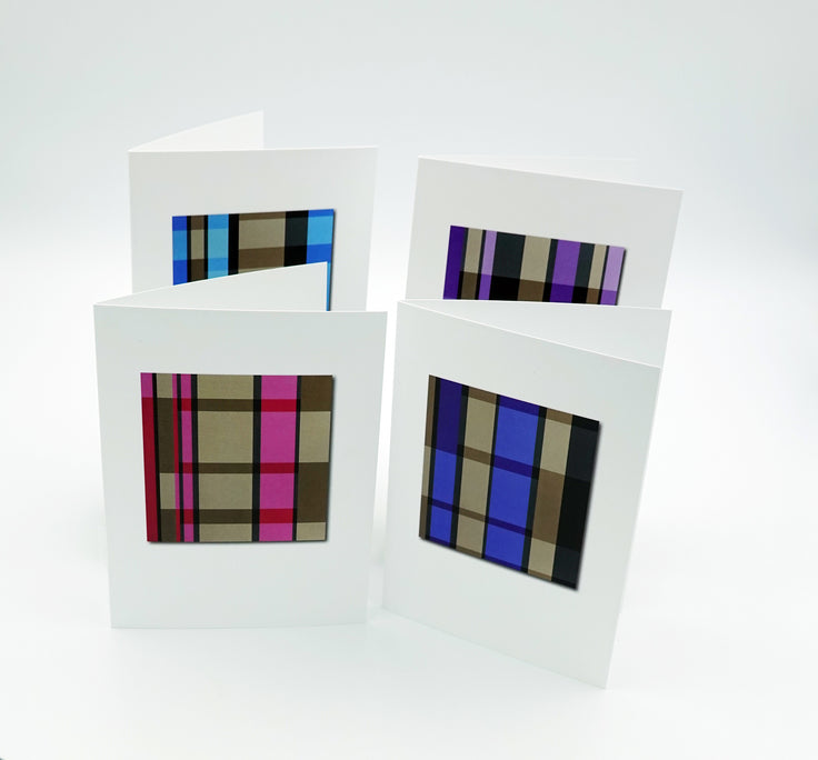 Four white greeting cards arranged in a cluster on a light gray studio background, each featuring a rectangular window with a different plaid pattern in blue, purple, brown, black, and pink.