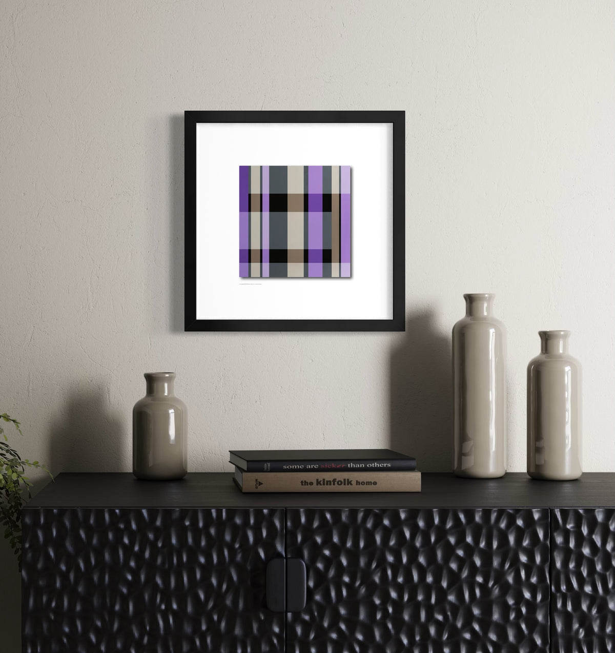 A framed abstract contemporary art print with a spiritual story featuring a purple, black, and beige plaid pattern, displayed on a light gray wall above a dark textured cabinet with decorative vases and books.