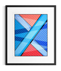 Framed abstract geometric wall art about the search for meaning featuring intersecting diagonal bands and striped sections in blue, red, and light blue, presented in a black frame with a white mat against a light gray background.