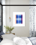 A framed contemporary abstract art print featuring a colorful plaid pattern in shades of blue, purple, orange, and pink, displayed in a white frame on a light gray wall above a bed in a modern bedroom setting.
