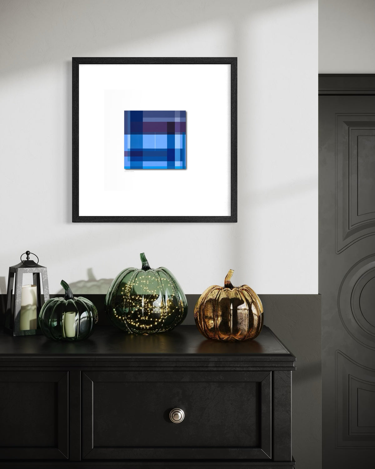 A contemporary spiritual framed abstract art print featuring a blue and navy plaid pattern, displayed on a white wall above a black wooden console table with decorative pumpkins.
