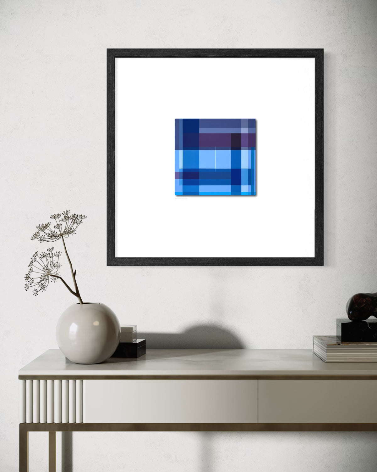 A contemporary spiritual square framed wall art print featuring an abstract geometric pattern in shades of blue and purple, displayed on a light gray wall above a console table with a vase and books.