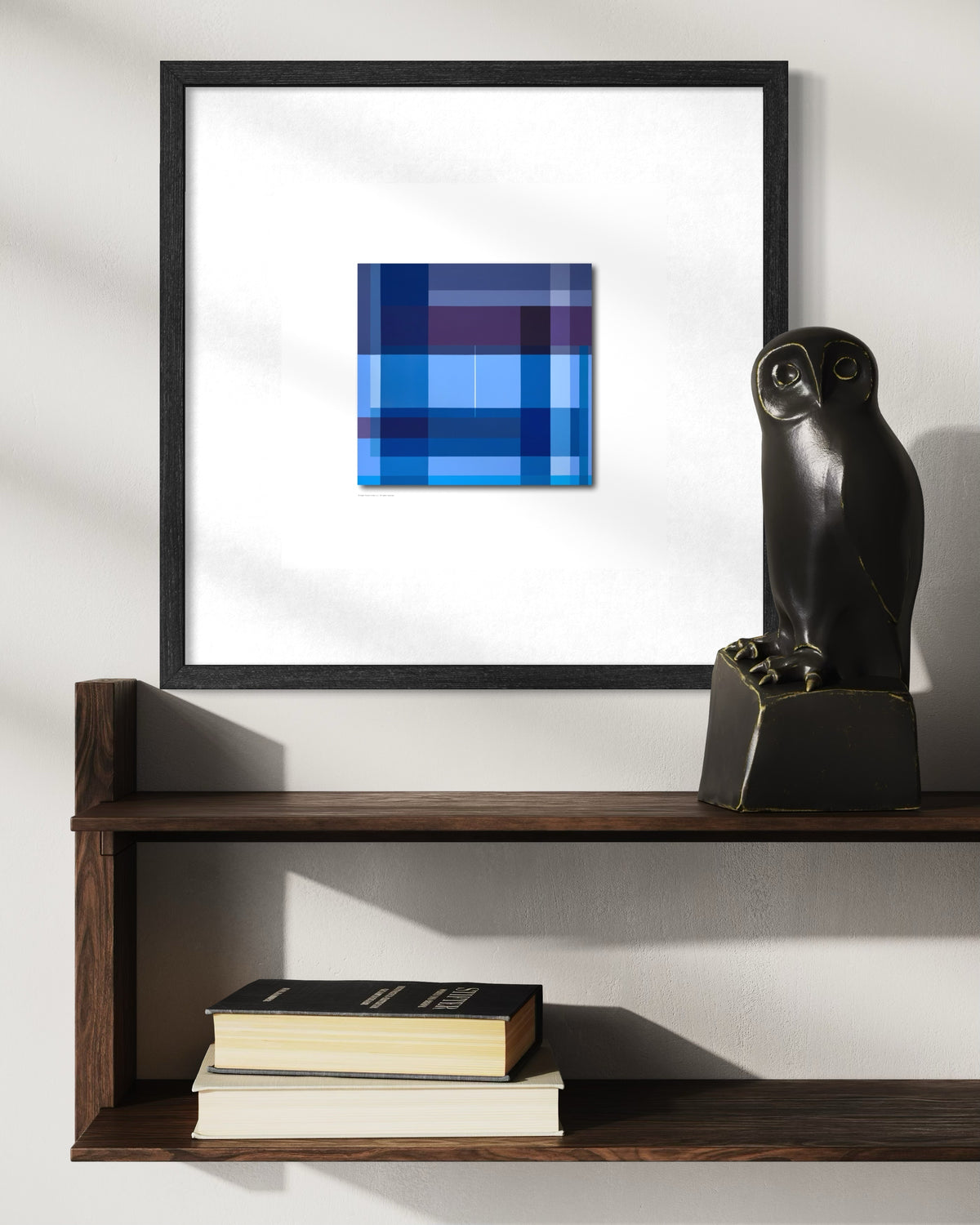 A framed contemporary abstract spiritual  geometric art print featuring shades of blue, navy, and purple, displayed on a white wall above a dark wood shelf with books and a black owl sculpture.