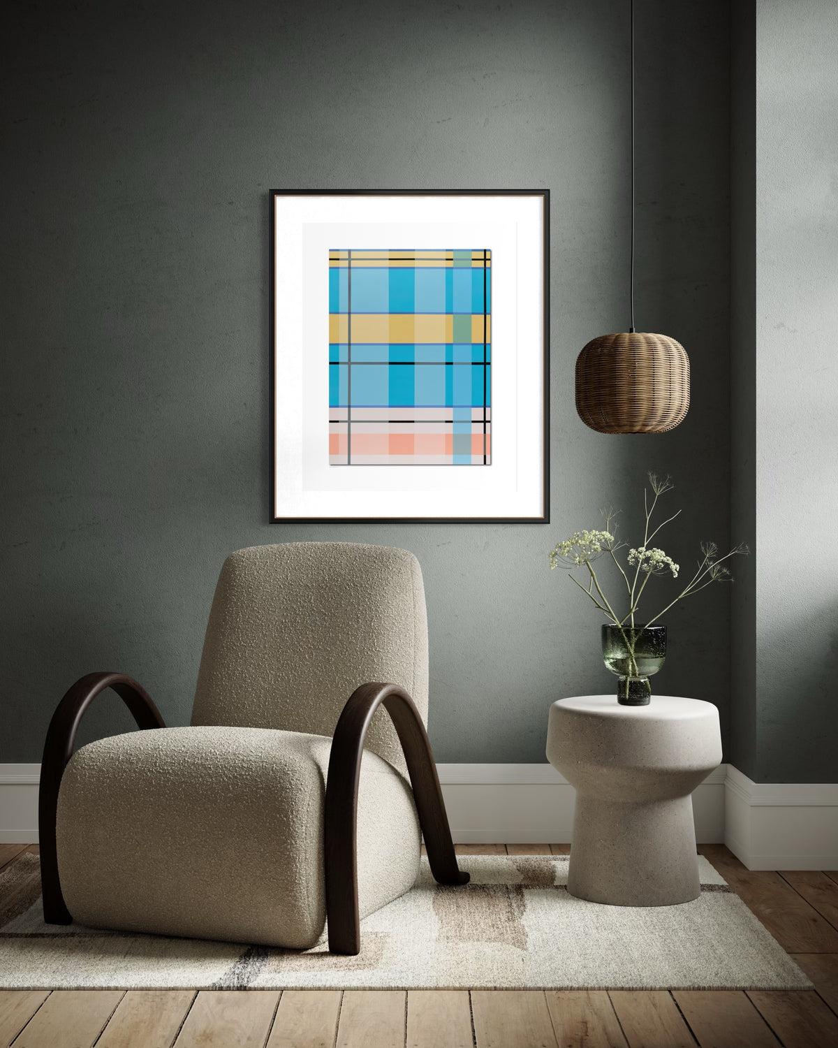 A framed abstract geometric art print with blue, yellow, and pink plaid-like blocks hangs on a dark gray wall above a beige armchair and a small side table with a vase of flowers.