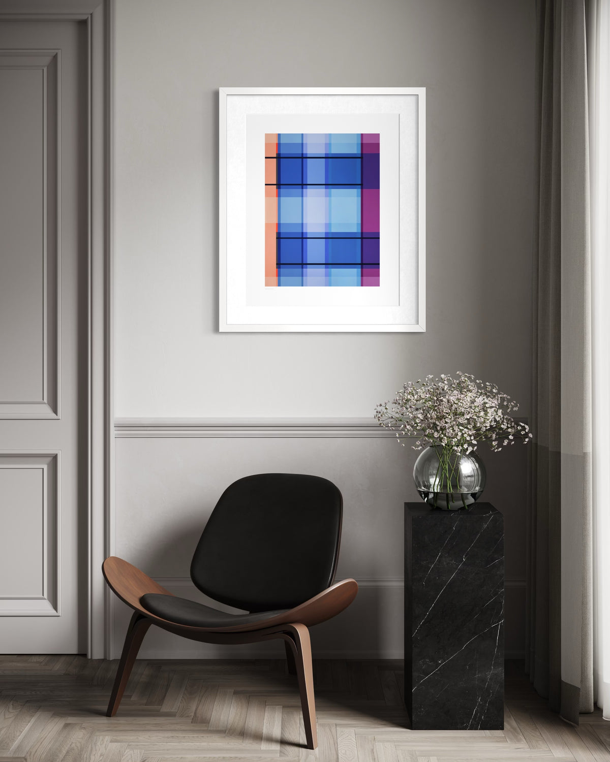 A framed contemporary abstract plaid art print with blue, purple, orange, and pink shapes, displayed in a white frame on a gray wall in a modern room setting above a black and wood chair.